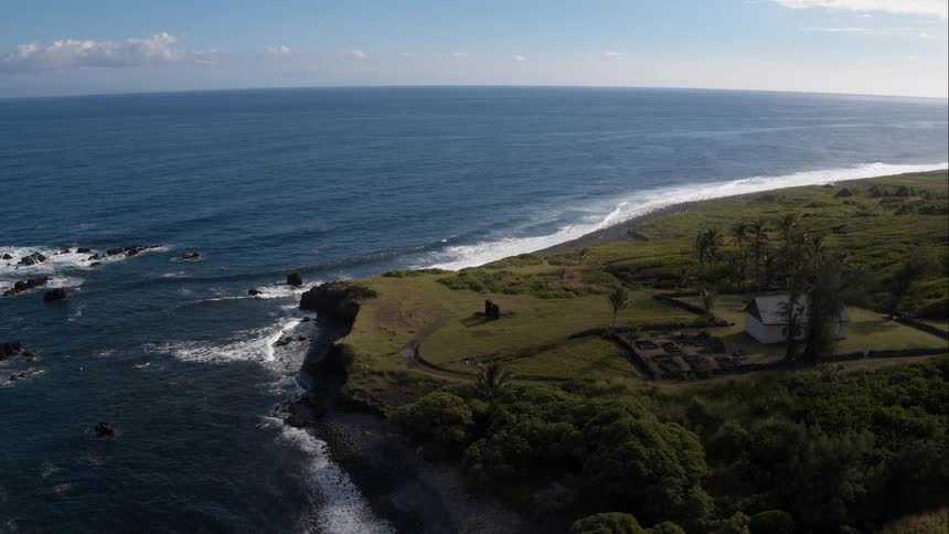 Waves crash into the shore that leads to green fields sparsely populated with trees