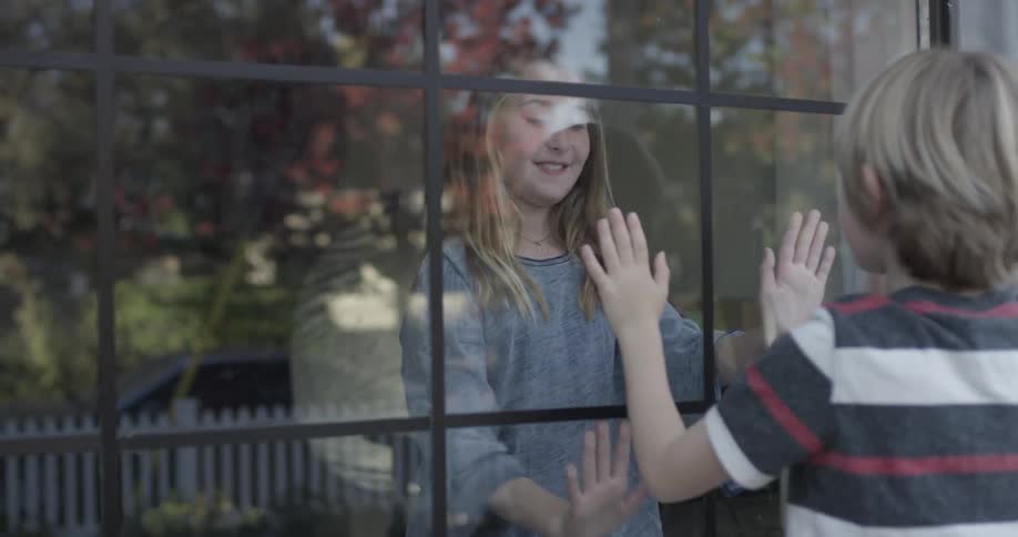 Two children play hand games through a window