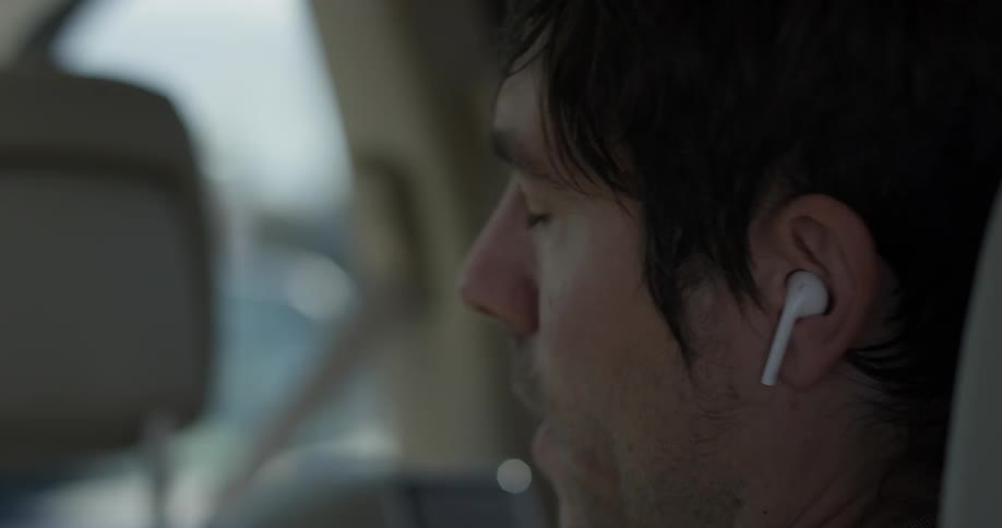 A man in the back seat of a car puts in ear buds
