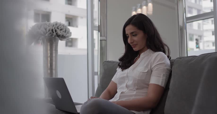 A woman types on a laptop as she sits on a couch