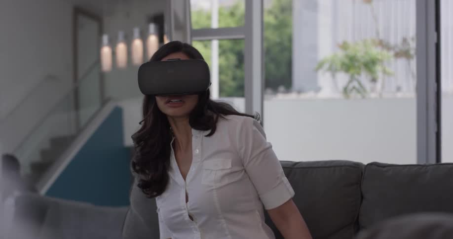 A woman wearing vr glasses flinches and swipes her hands while sitting on the couch