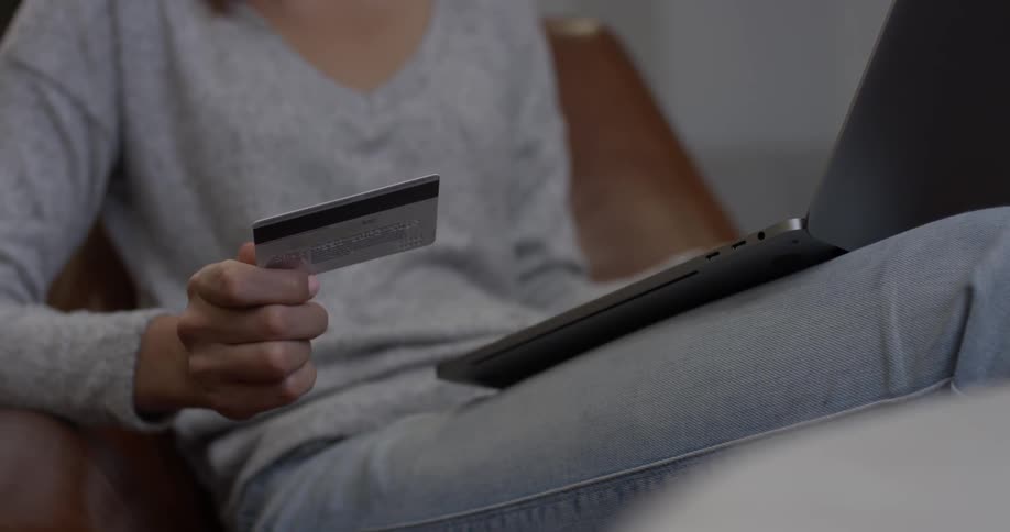 Woman looks at a credit card and types on a laptop