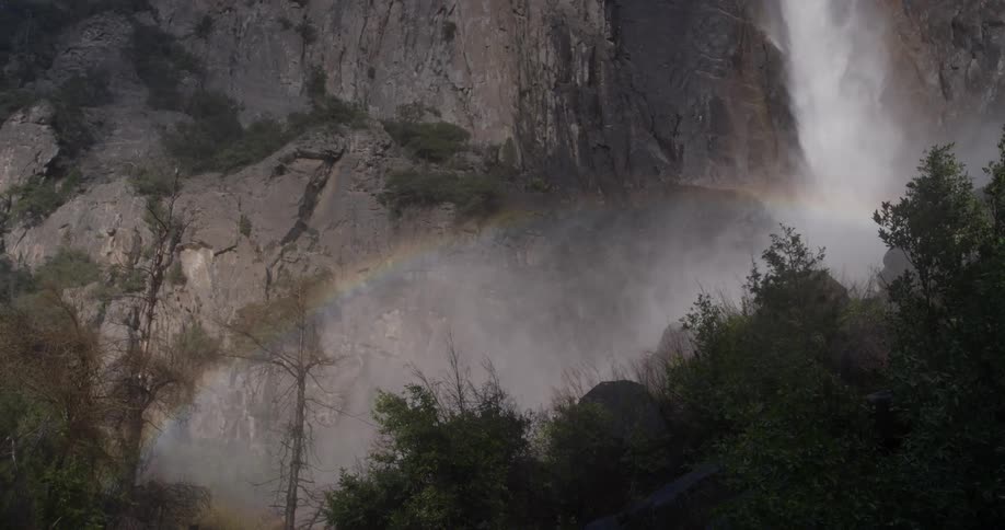 A waterfall crashes to the rocks below spewing mist all over trees and creates a rainbow