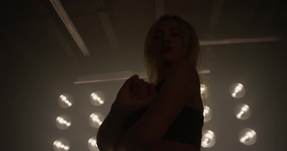 A woman performs a dance in front of large lights