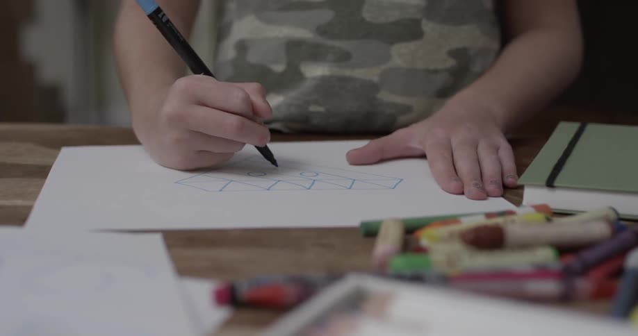 Person drawing pictures on a crayon and marker covered table