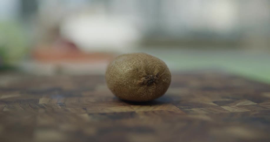 Kiwi is violently chopped in half on top of a cutting board by a very sharp knife