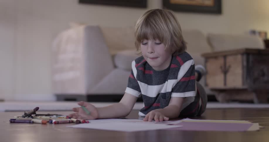 Young boy lying on the floor coloring at home