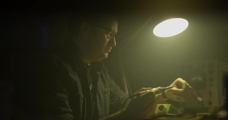 A man sits at a table and picks up a solder gun