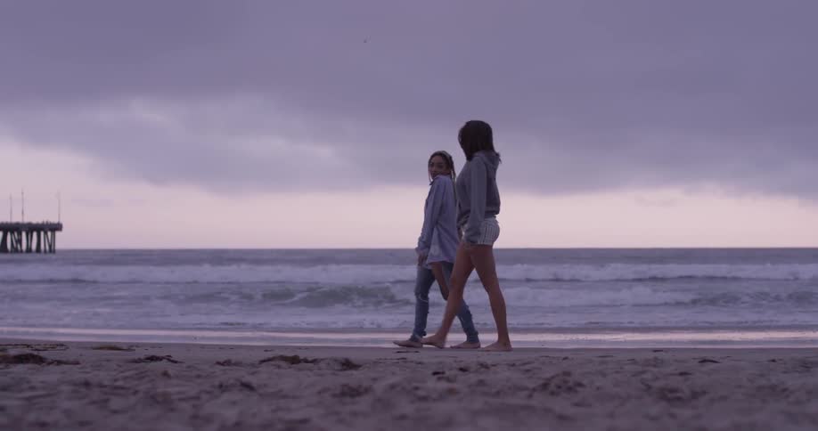 Two women walk along a beach on an overcast day