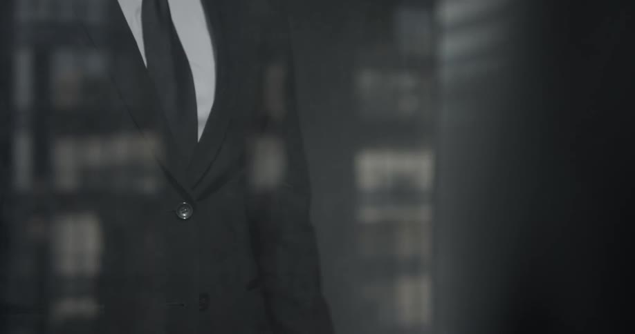 Man buttons suit jacket using window as a mirror