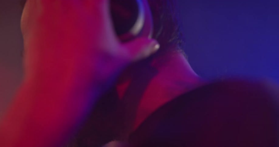 A man is doing a dj performance at a club up on stage wearing headphones with red and blue lights shining on him