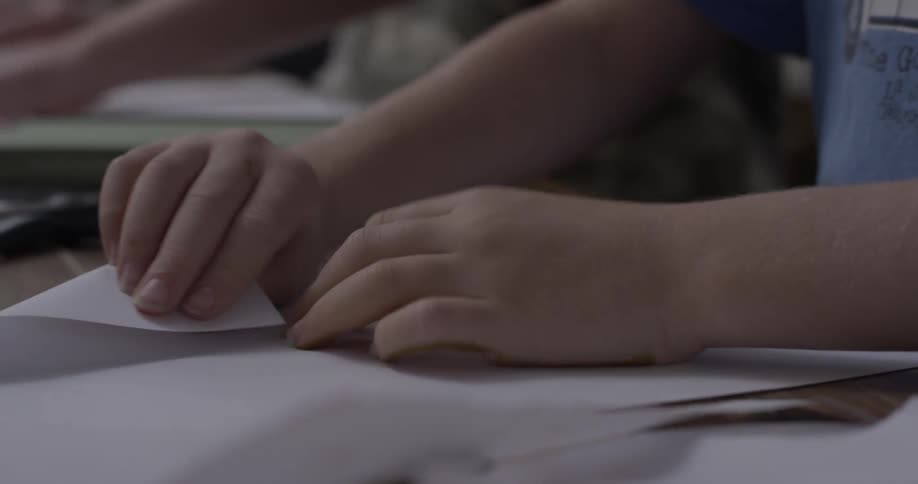 Two children fold pieces of paper on a table