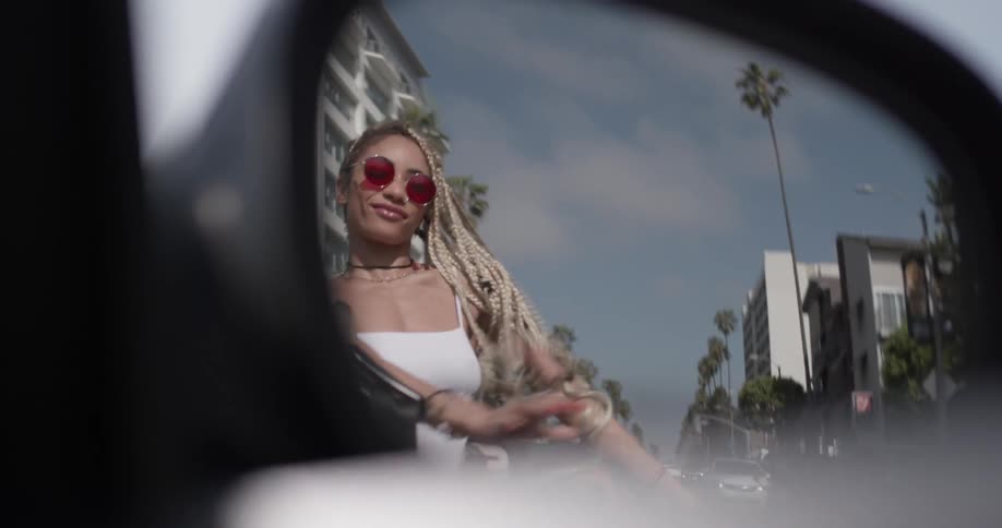 A convertibles side mirror reveals a woman dancing in the back seat