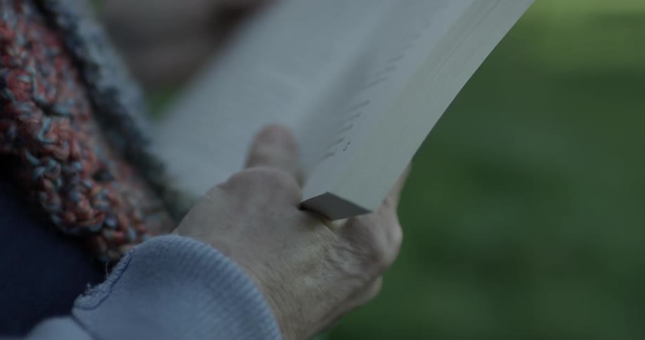 An old woman reads a book outside on the grass