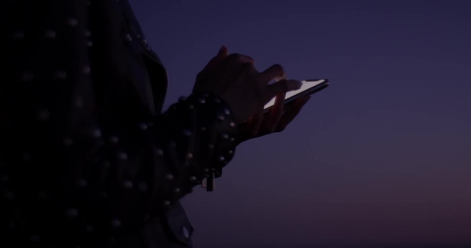 Someone plays on their phone in the darkness as the sun sets