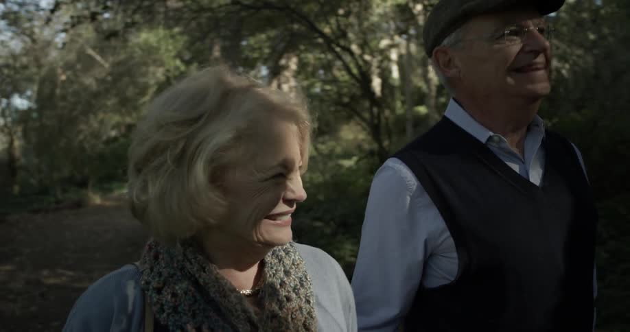 An older couple laugh and smile as they walk through a forest