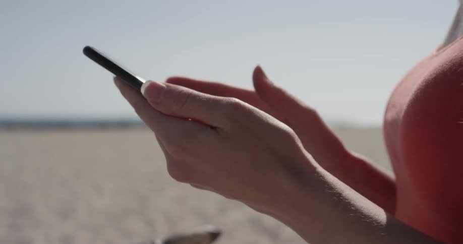 Woman taps on a phone while standing on the beach