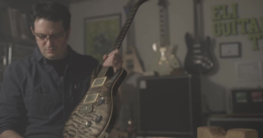 A man flips a guitar in his hands then plugs it in