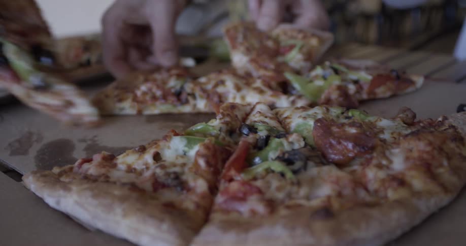 Pizza is served to many people by the slice with black olives and green peppers