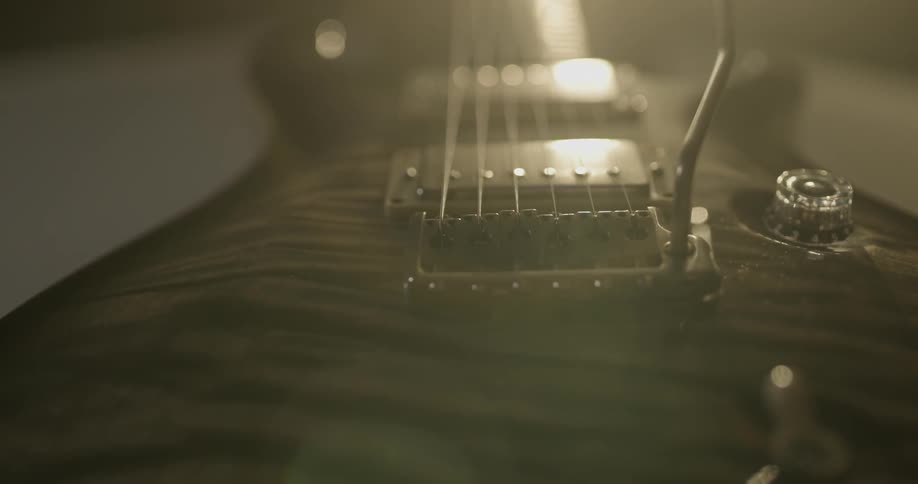 An electric guitar is shown in a small light in a dark room