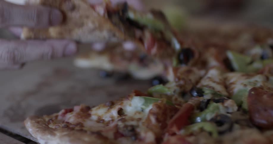 Two people's hands grab slices of pizza from a pie