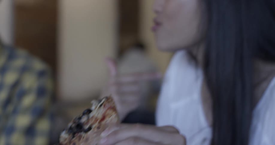 Woman eats pizza while gesturing with hands and talking