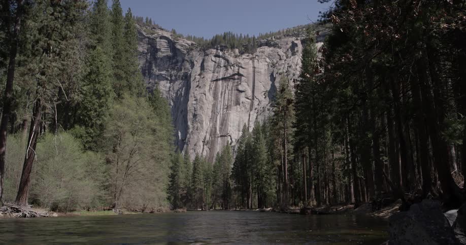A beautiful landscape of a tall mountain face with trees and a river