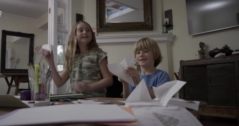 Two children fly paper airplanes indoors