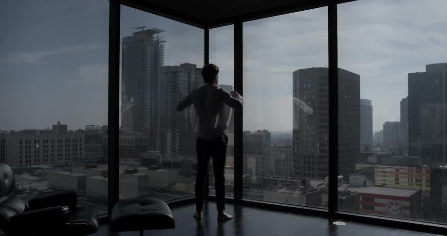 Man finishes dressing as he walks up to a wall of windows
