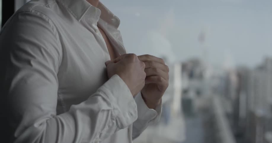 A man buttons his shirt while overlooking the city
