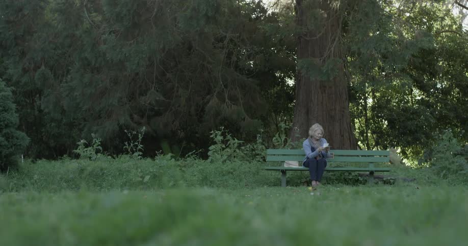 Woman sits on bench outside while looking at something