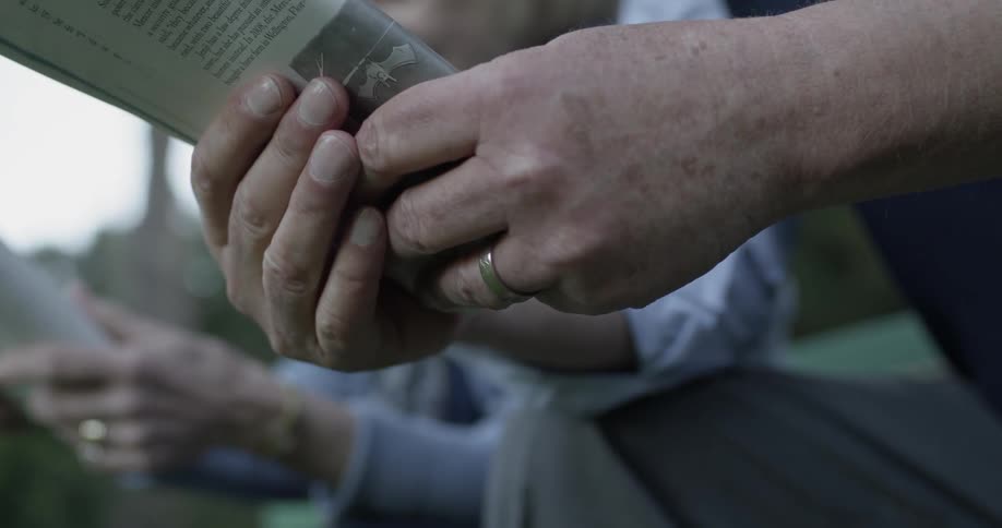 An older man and woman sit outside and read next to one another