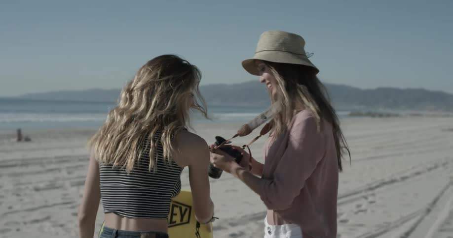 A woman wearing a hat taking a picture of another woman and laughing with hers