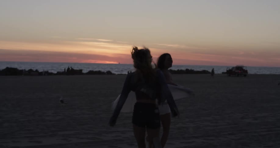 Two women run playfully on the beach toward the sea,