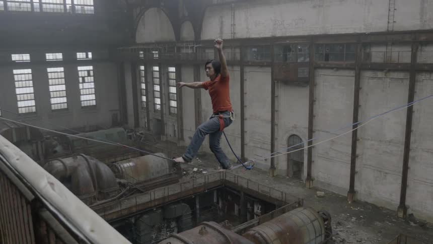 A man in an abandoned factory attempts to walk a tightrope and loses his balance
