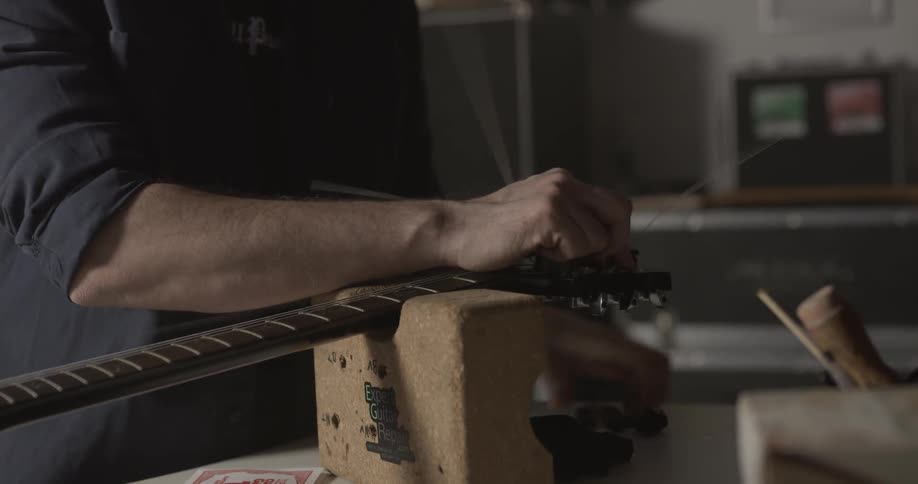 A man strings a guitar that's sitting on a table