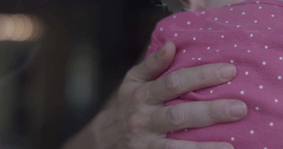 Someone holds a baby and strokes the baby's back with their thumb