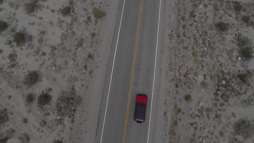 A red and black car drives down a road in the desert