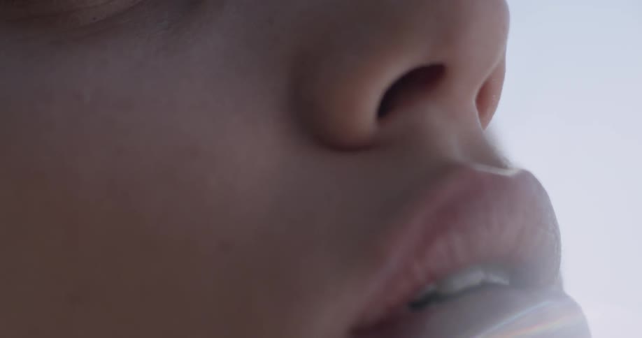 A close up of a woman and her lips is seen as a bright blue background with sunny skies appears after lifting her head