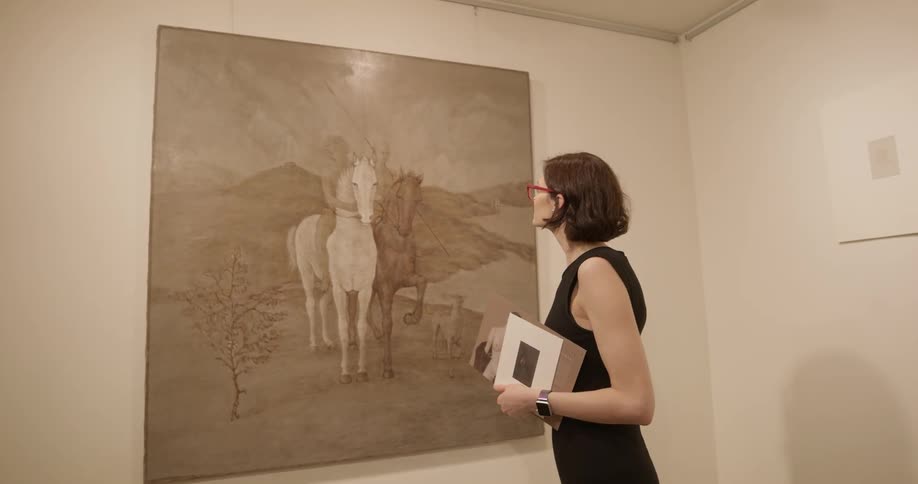 A woman is looking at a painting on the wall