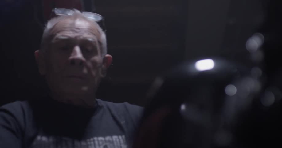 Male approximate age 6 mounts motorcycle turns the key black background black clothing reading glasses on top of his head