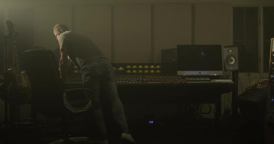 Man leans against a desk that has audio equipment on it