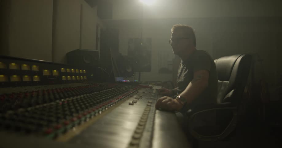 A man sits under a light adjusting knobs on a mixing board