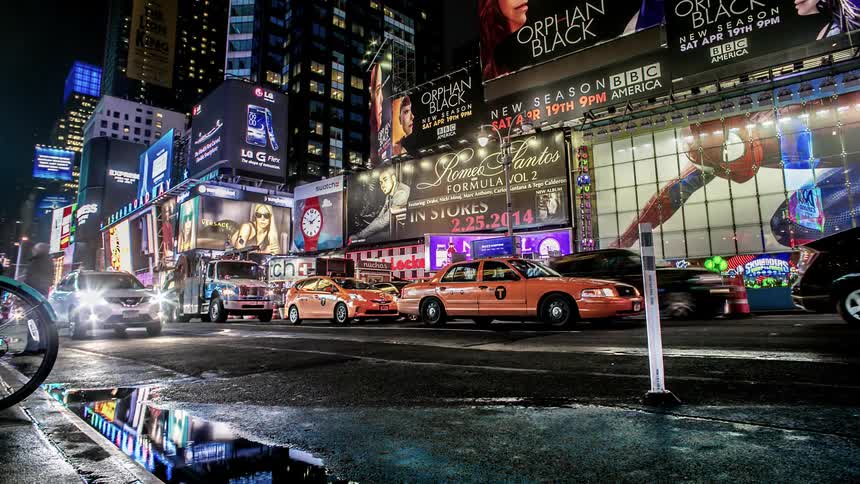 A busy city road with video billboards and lots of traffic and pedestrians
