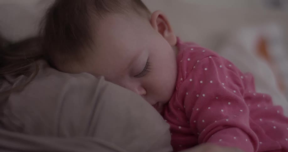 A baby in a pink outfit sleeps peacefully on a  woman's chest
