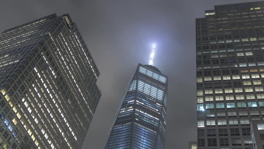 A lit skyscraper stands under clouds at night