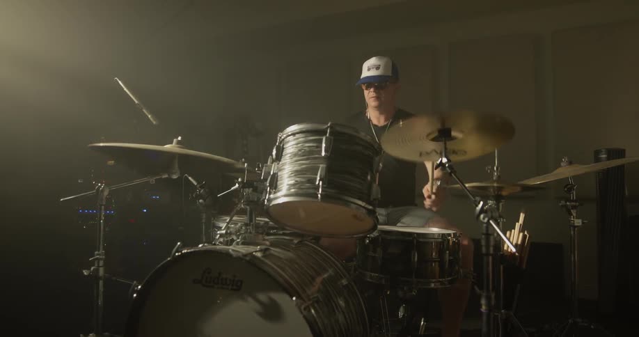 Man plays a drum set while wearing a baseball hat