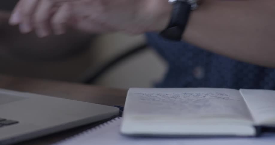 A man writes something in a notebook then types on a laptop