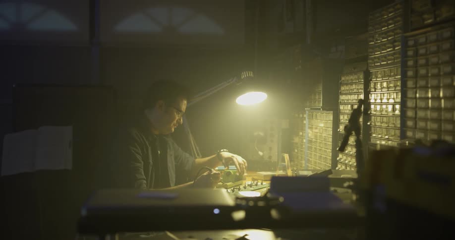 A man walks over to a workbench with a single light illuminating it