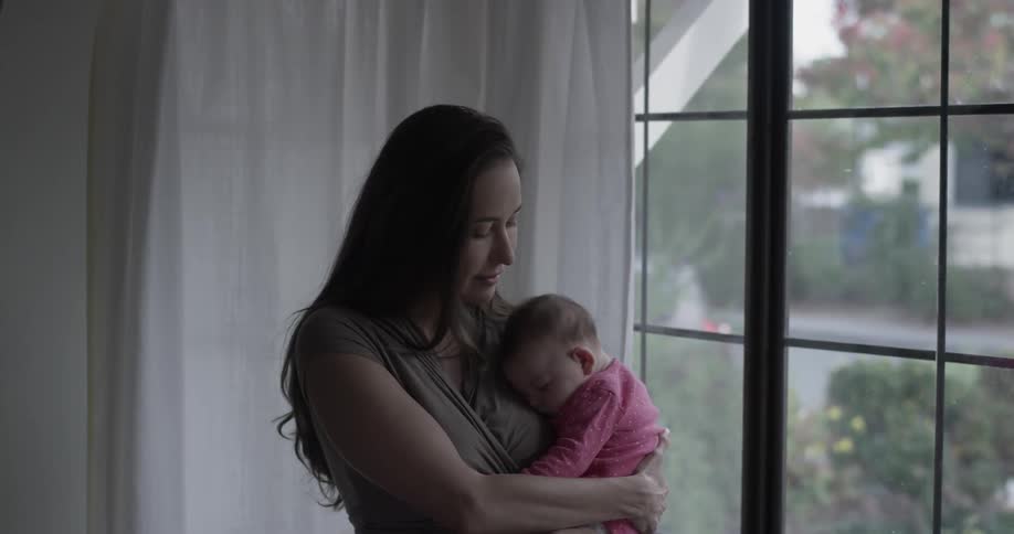 A woman holds a baby in front of a window